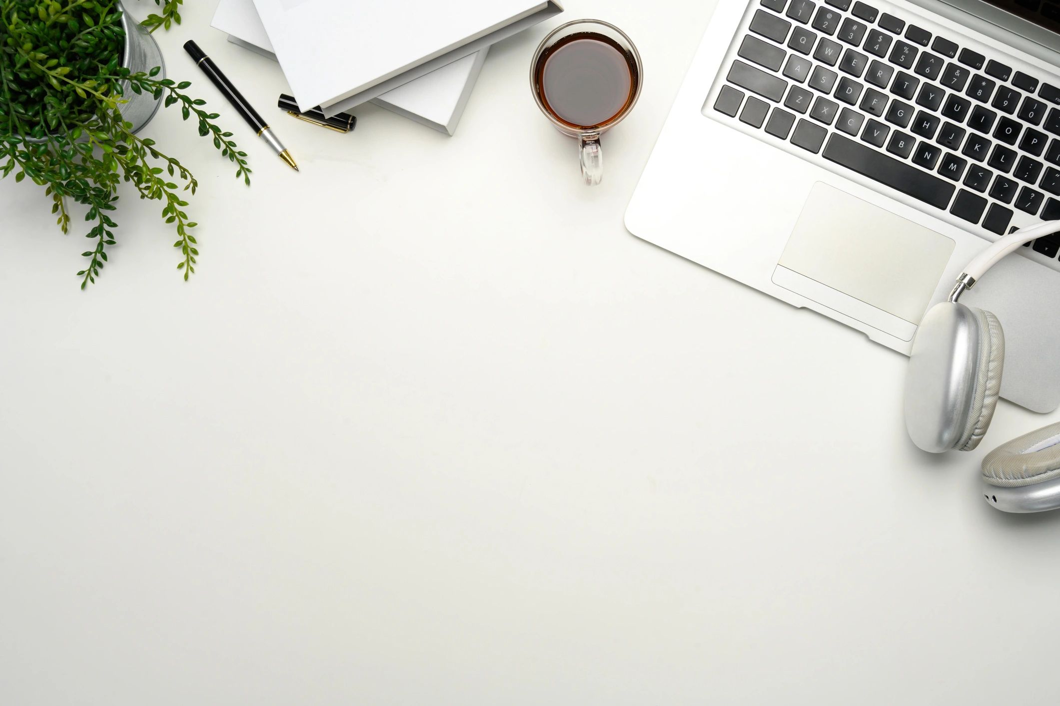 Minimalist workspace with laptop, coffee cup, headphones and notebooks on white desk